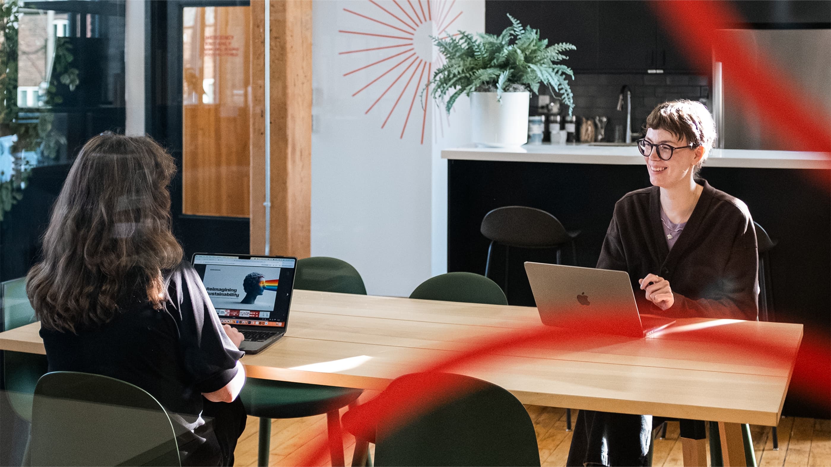 Two Works Design colleagues seated across each other with laptops open.