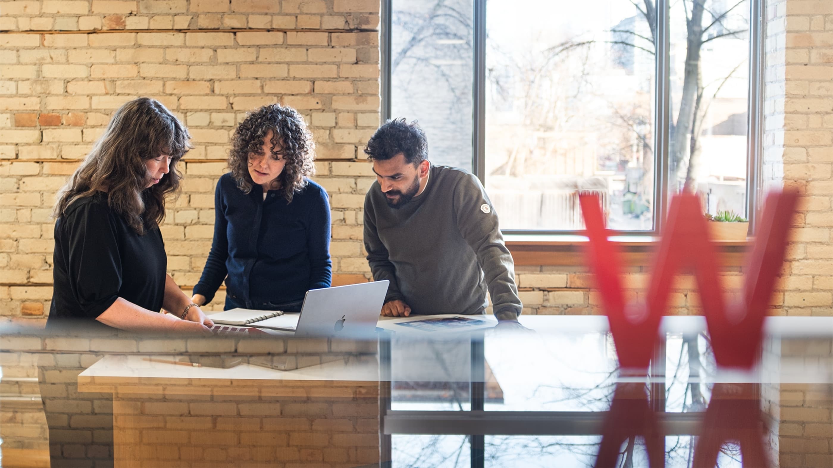 Three Works Design colleagues standing around a table with an open laptop on it, collaborating on a project.