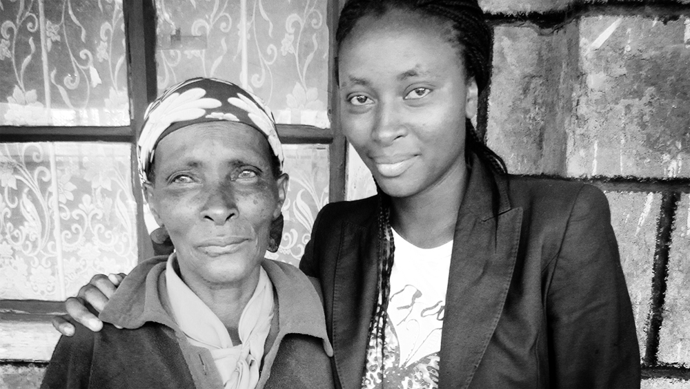 A mother and daughter stand with their arms around each other.