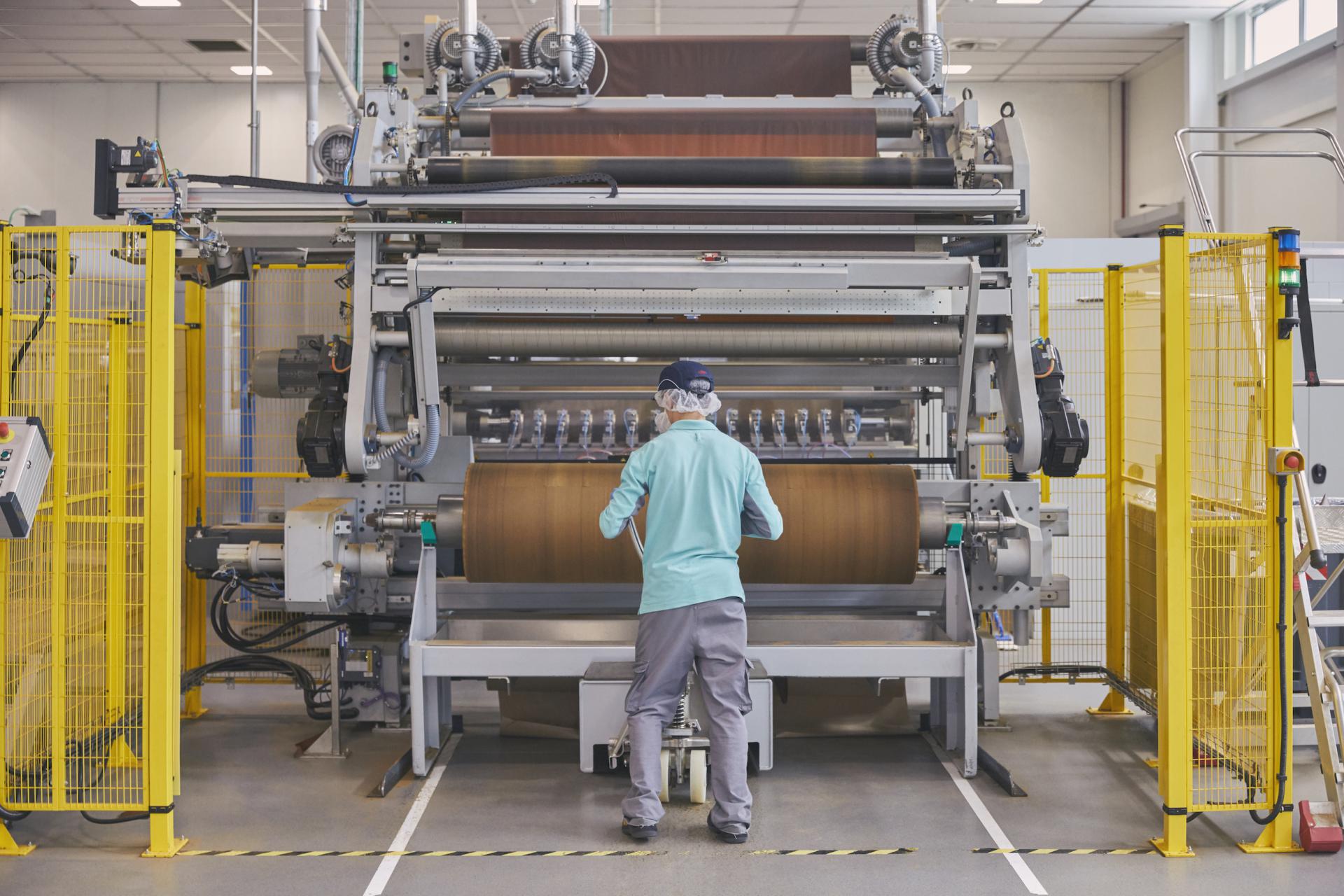 A man in a Phillip Morris factory oversees tobacco leaves running through a machine.