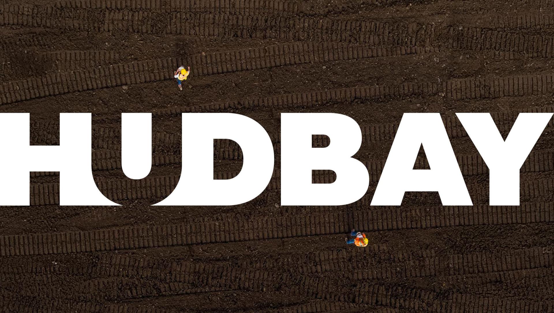 Overhead view of the Hudbay logo superimposed on top of dark soil with tire tracks.