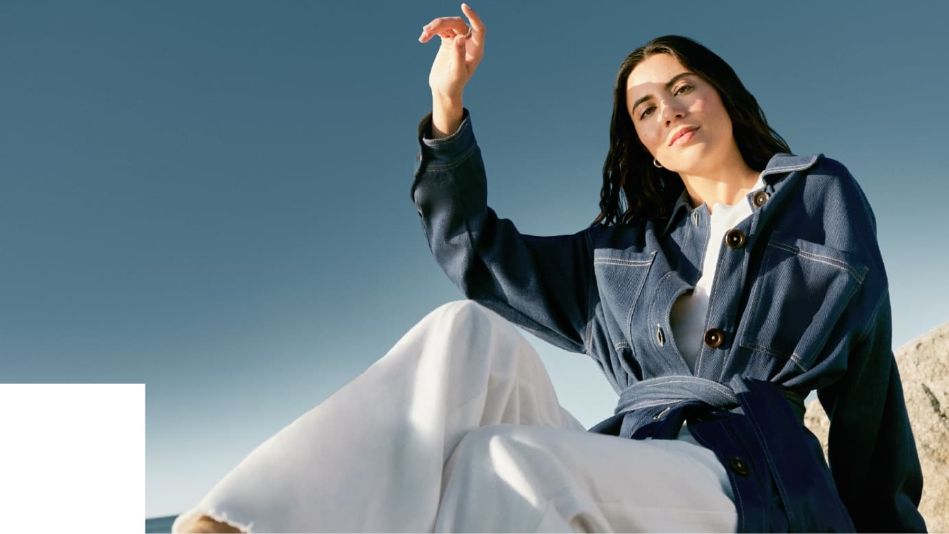 Image from Holt Renfrew’s 2024 Sustainability Report of a fashion model seated on boulders.