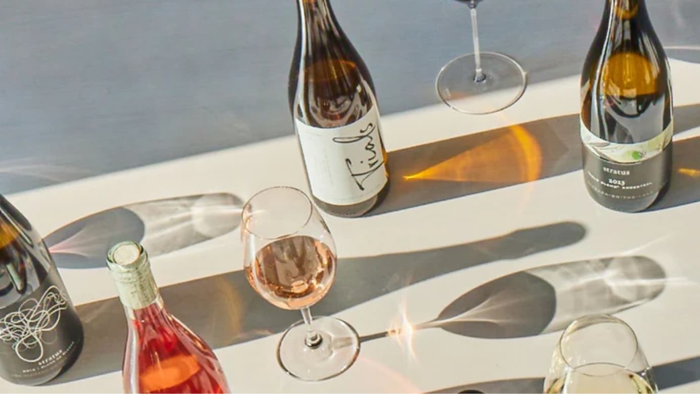 Four different wine bottles and two wine glasses on a table.