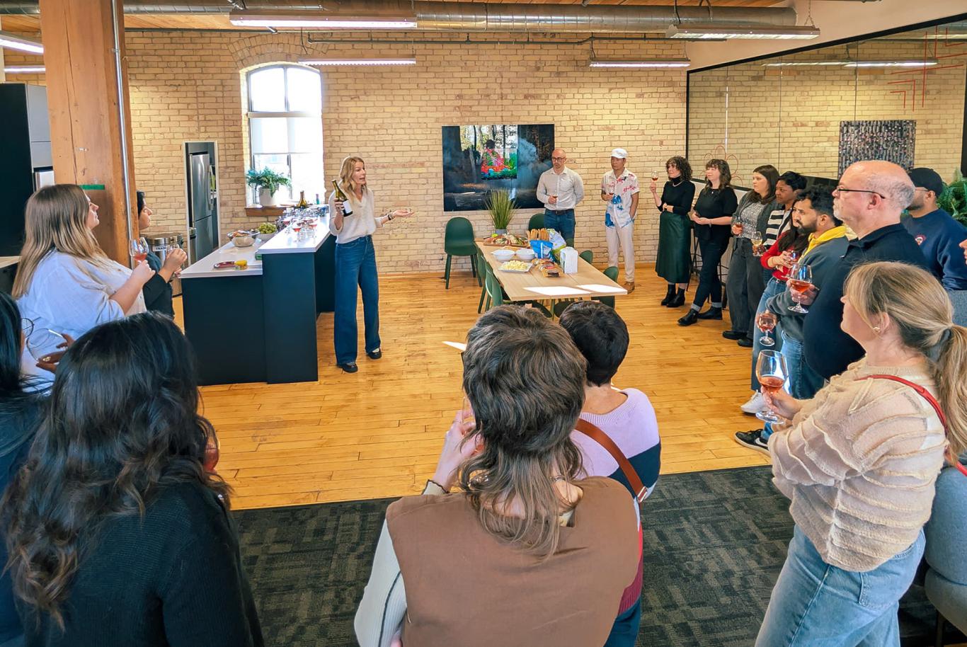 Works Design colleagues listen to a talk at a wine tasting event in the company’s office kitchen area.